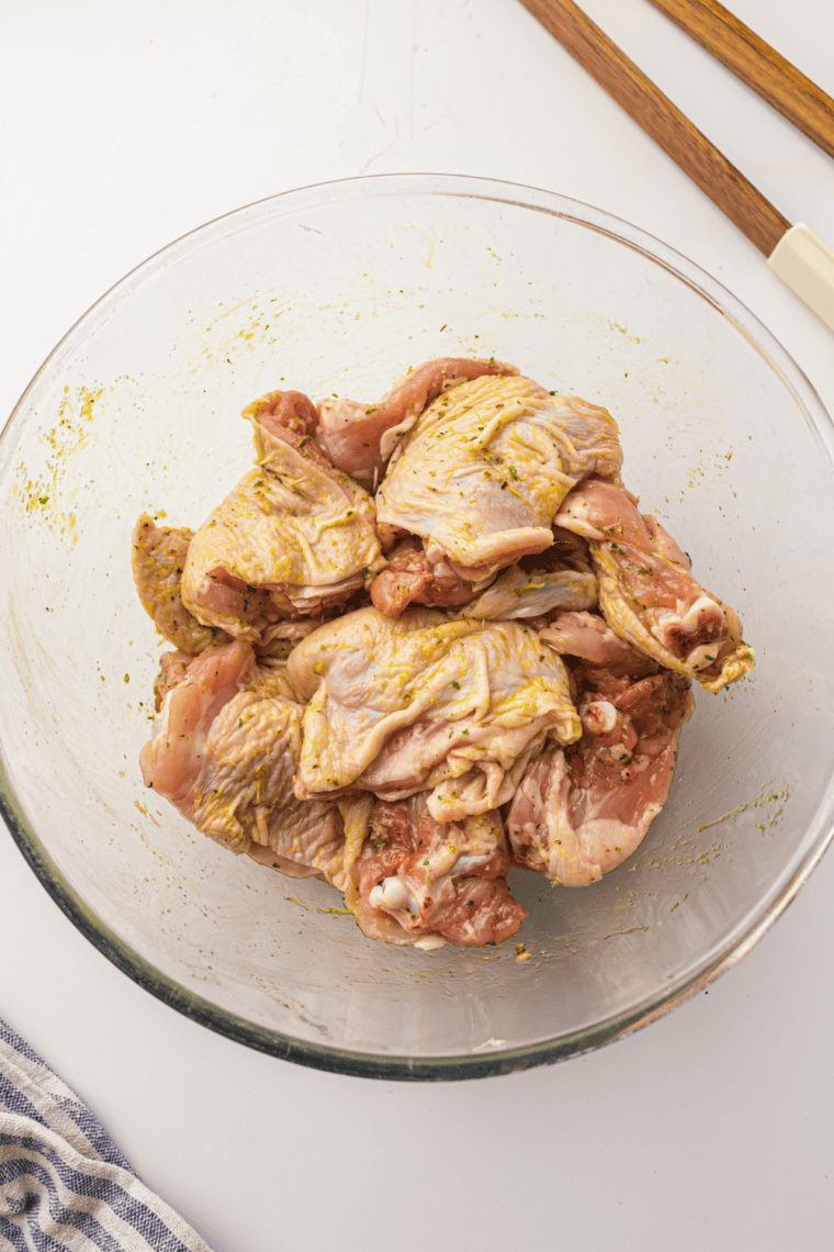Chicken thighs being rubbed with olive oil and sprinkled with spices.