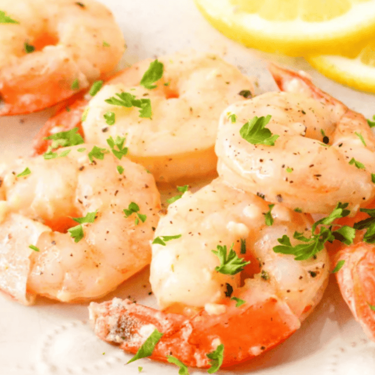 Pouring lemon garlic butter sauce over cooked shrimp in a serving bowl with lemon wedges.