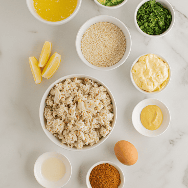 Lump crab meat, panko, Old Bay, Dijon mustard, mayonnaise, and egg in glass bowls for air fryer crab cakes.