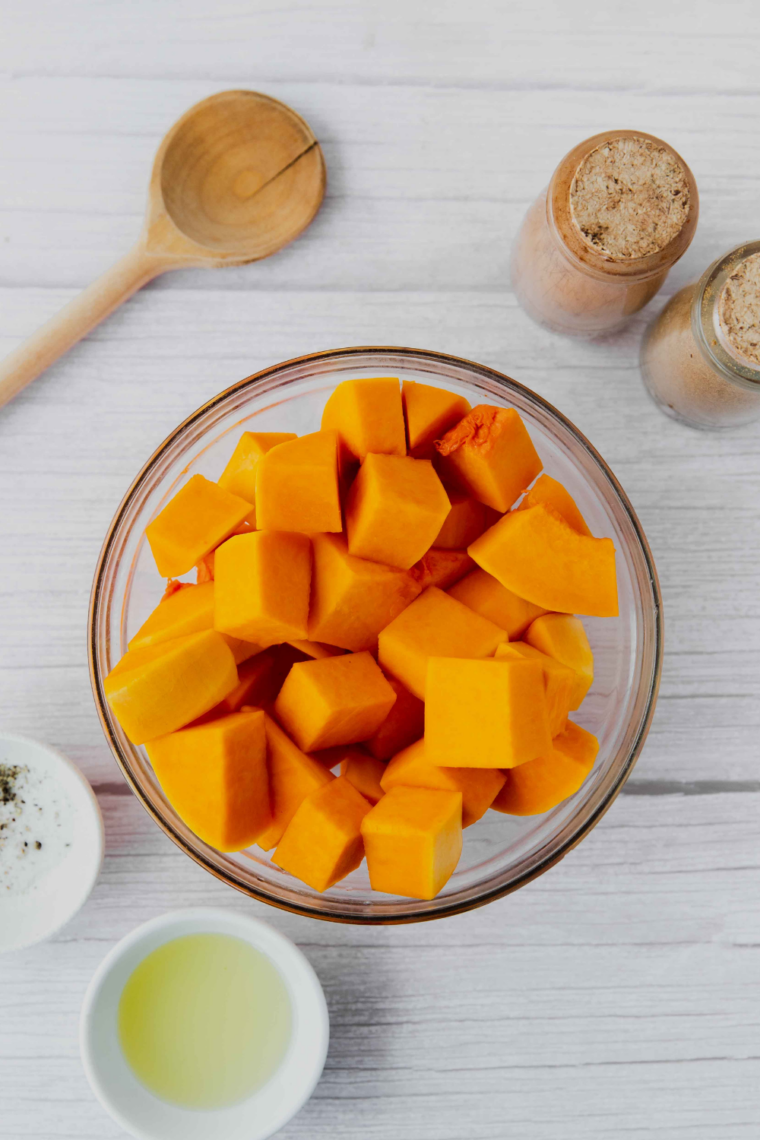 cubed butternut squash tossed with olive oil and herbs evenly coated in bowl