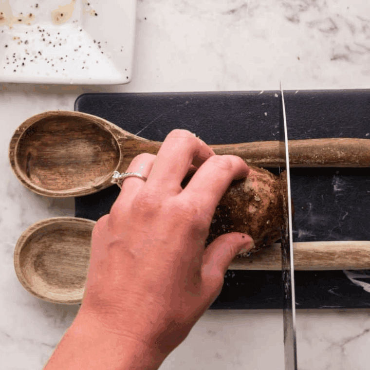 Slicing potatoes thinly for Hasselback style using a rack or wooden spoons, ensuring slices don’t cut all the way through