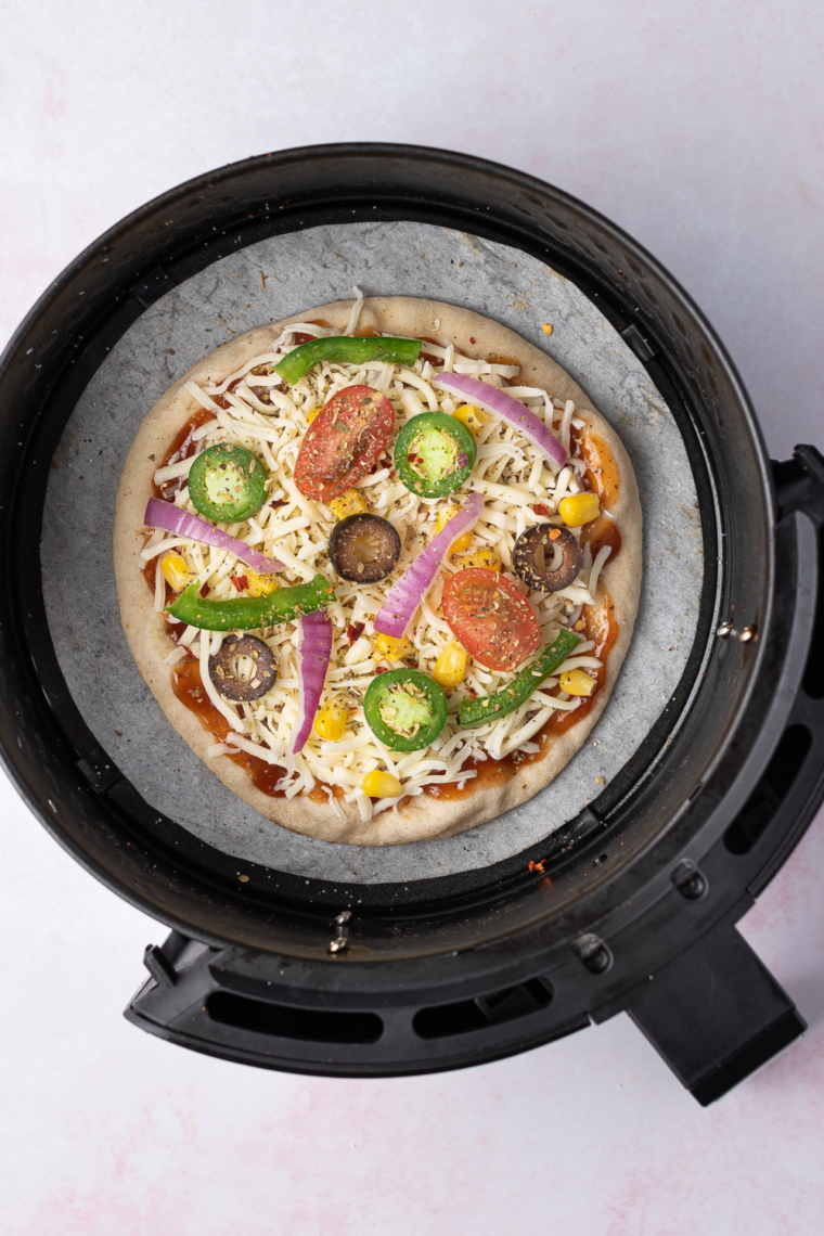 Pita pizza cooking in an air fryer at 360&deg;F with bubbling melted mozzarella cheese and crisp golden edges