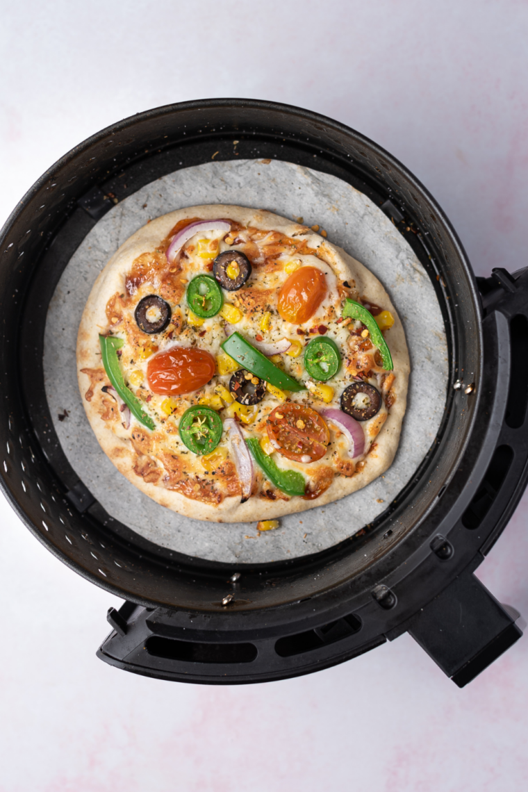 Sliced air fryer pita pizza garnished with fresh basil and red pepper flakes, resting on a wooden cutting board