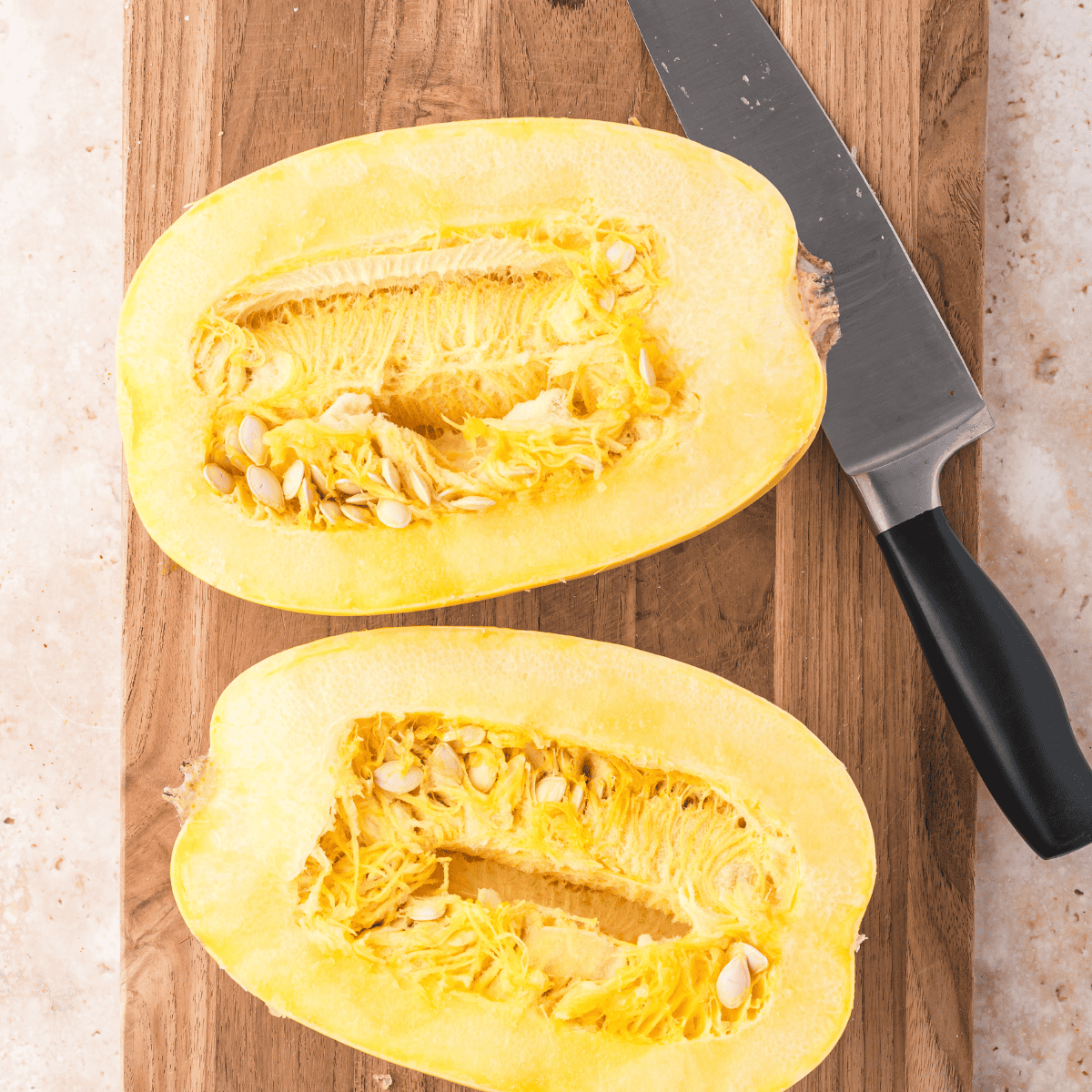 Cutting a spaghetti squash in half lengthwise with a chef's knife on a damp kitchen towel