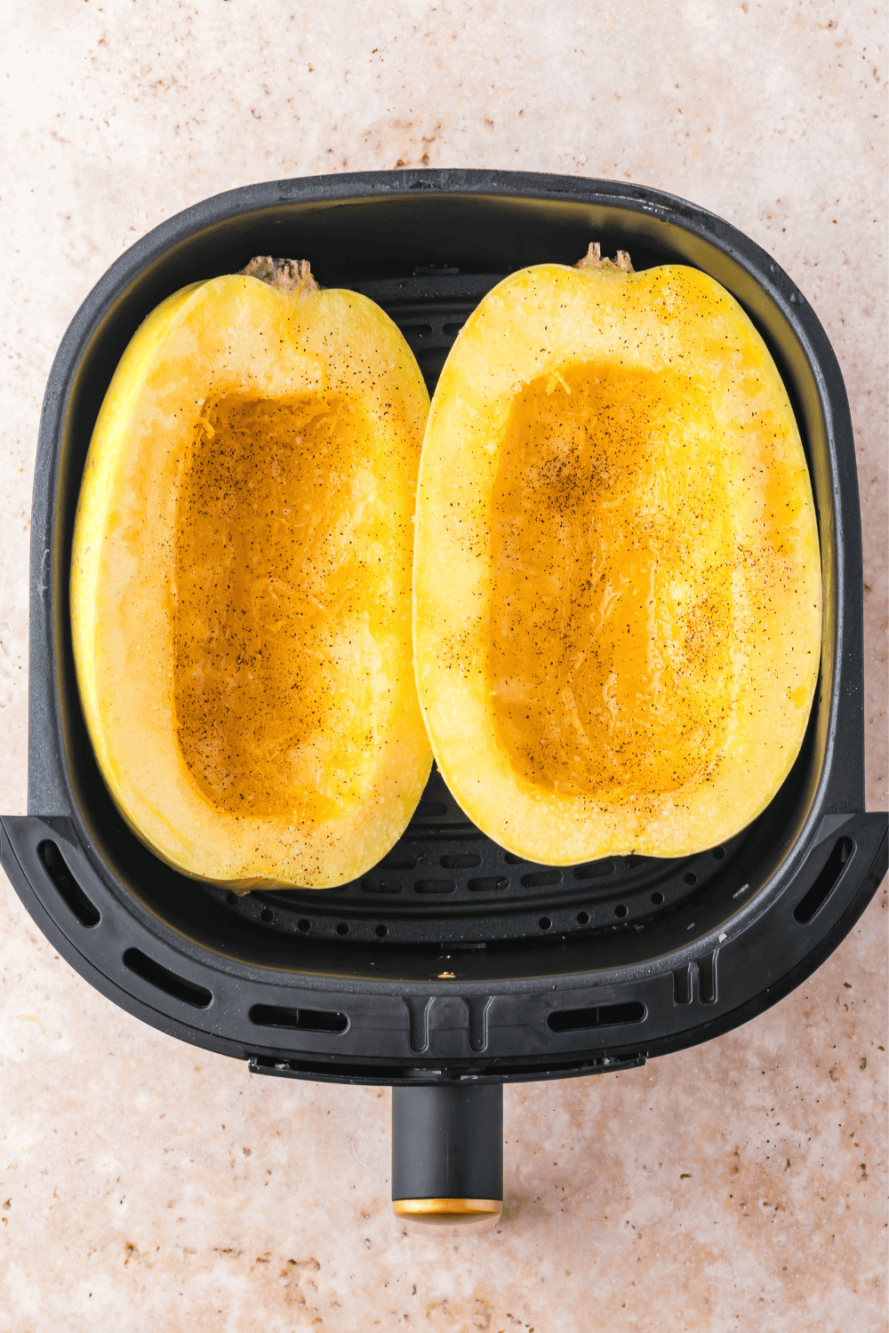 Two spaghetti squash halves placed cut side up in an air fryer basket