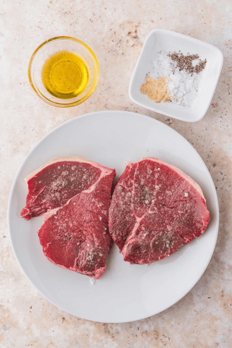 Raw sirloin steaks on cutting board, patted dry and seasoned with salt and black pepper.