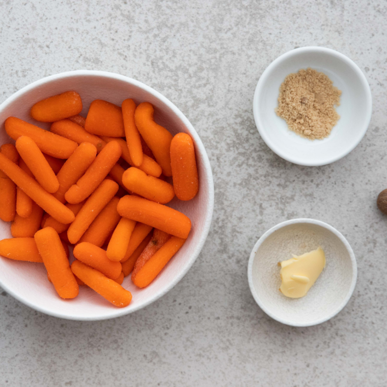 Ingredients for Bob Evans carrots on a kitchen counter, including baby carrots, unsalted butter, dark brown sugar, kosher salt, and fresh parsley.