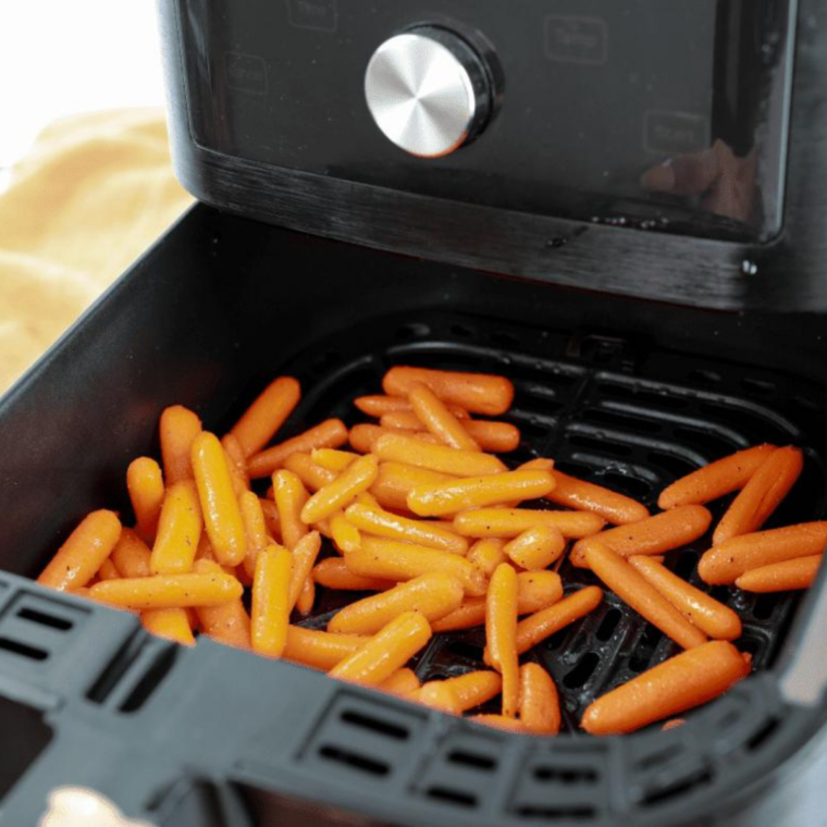 Brown sugar glazed baby carrots in a single layer in the air fryer basket, lightly browned on the edges.