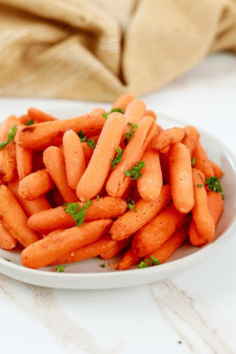 Copycat Bob Evans carrots in a white bowl, glazed with butter and brown sugar and topped with chopped fresh parsley.