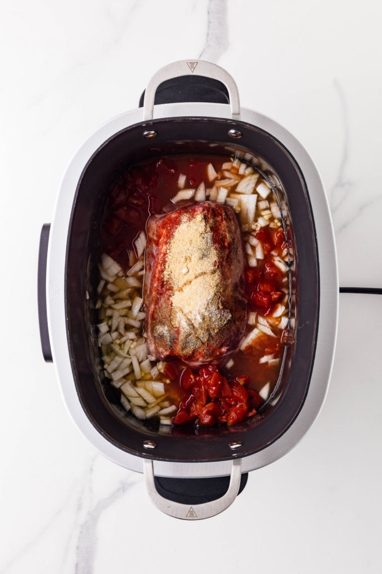 Seasoned pork shoulder on a bed of sliced onions in a slow cooker