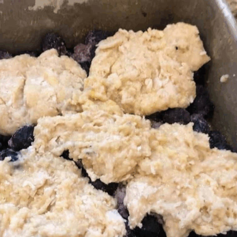 Greasing an air fryer-safe pan, adding blueberry mixture, and spooning cobbler batter on top before baking.