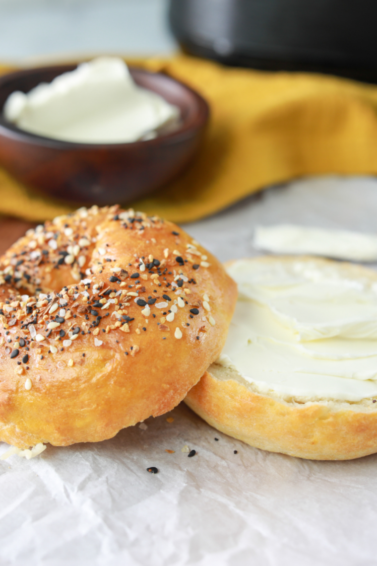 Four homemade air fryer everything bagels on a wooden board with bowl of cream cheese alongside