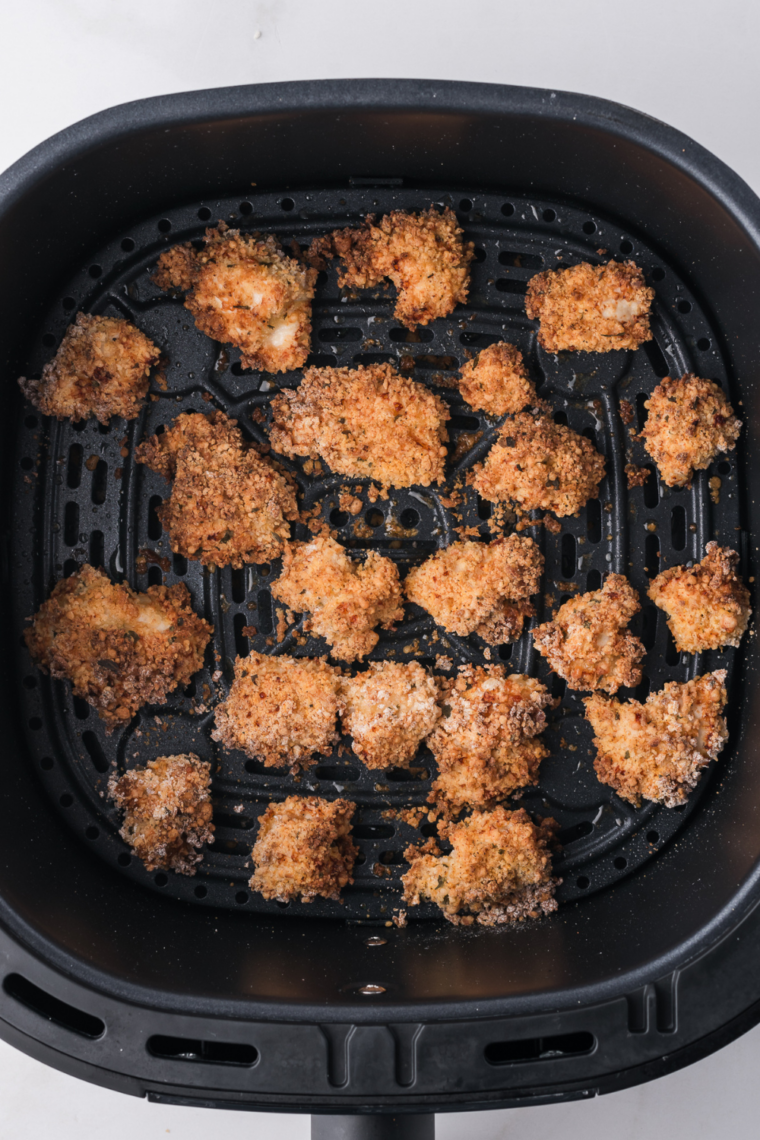 Garlic parmesan chicken bites turning golden brown in the air fryer basket partway through cooking
