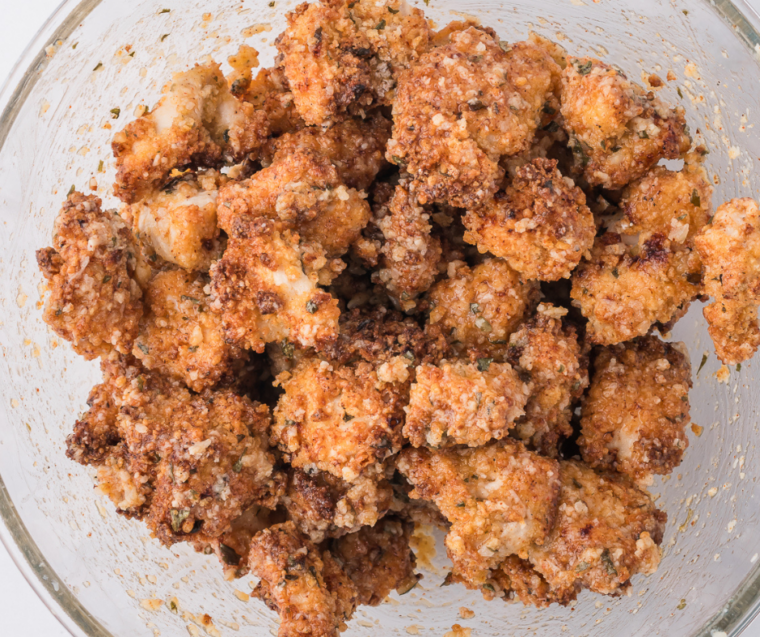 Cooked chicken bites being tossed in garlic butter parmesan sauce in a mixing bowl