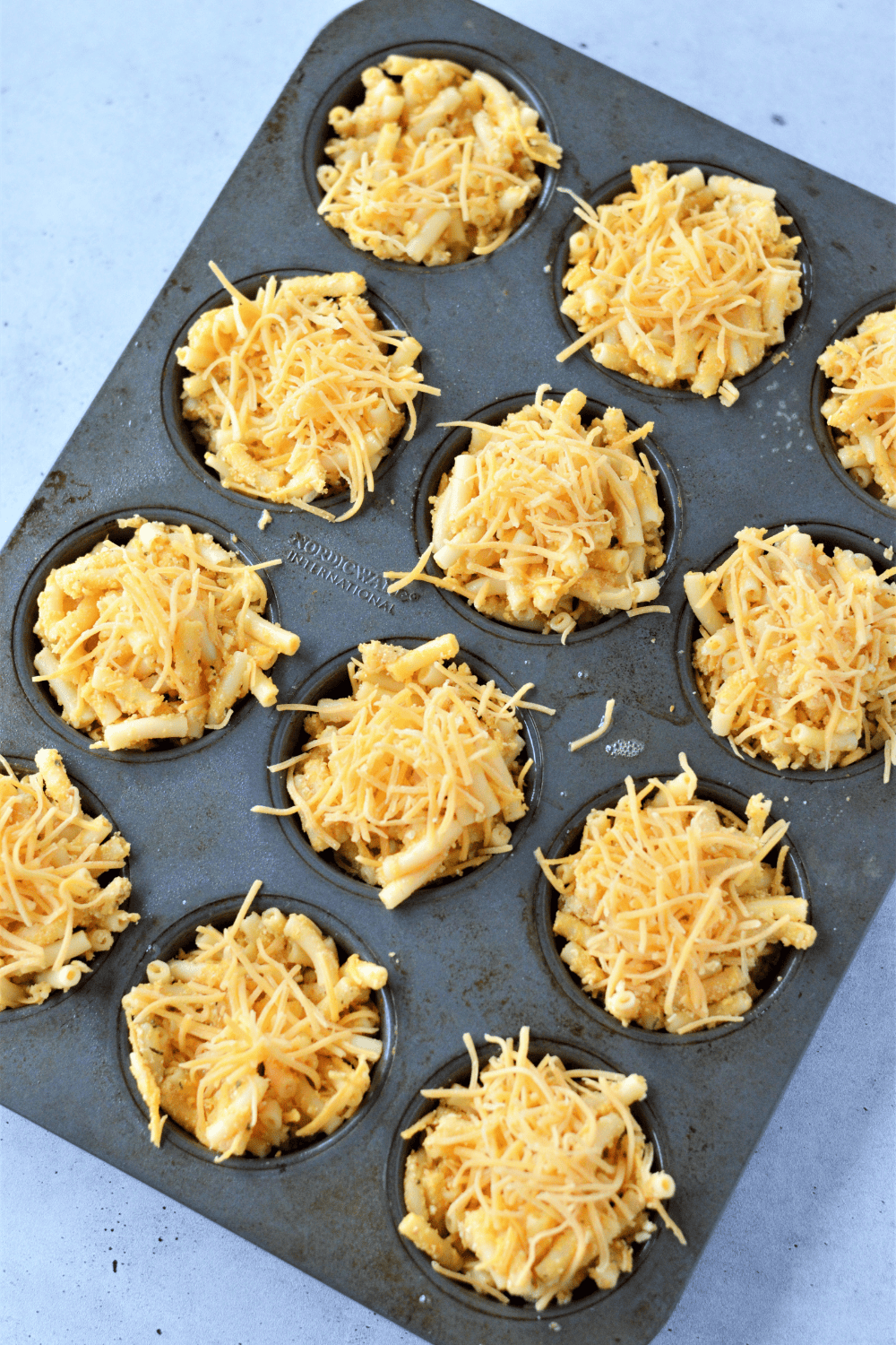 spraying muffin tin and filling each cup with macaroni and cheese mixture