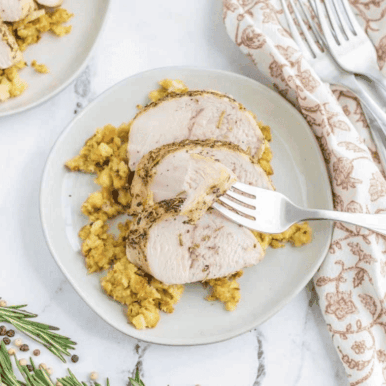 Golden-brown air fryer turkey tenderloin sliced on a platter with fresh herbs and a side of roasted vegetables.