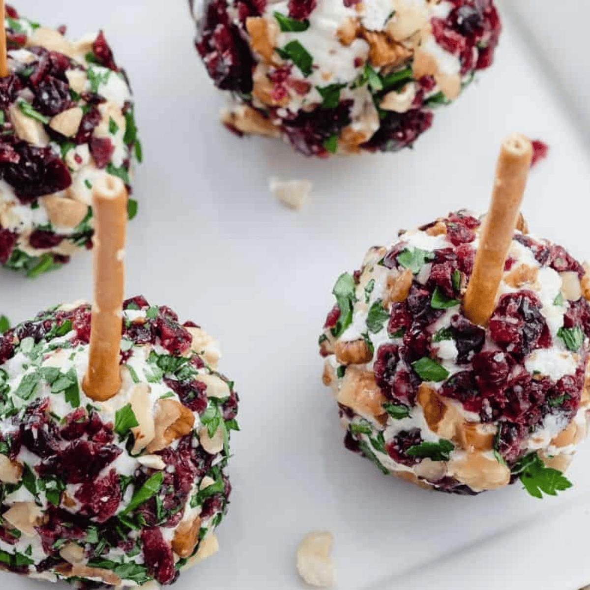 Cranberry Pecan Cheese Ball on a serving plate, coated with chopped pecans and fresh herbs.
