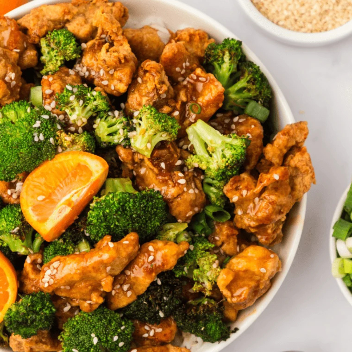 serving air fryer orange chicken over rice with sesame seeds and green onions
