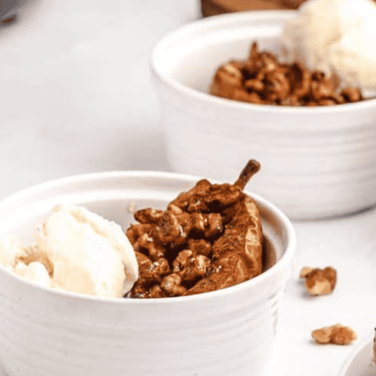 Air fryer baked pears topped with cinnamon, chopped nuts, honey, and vanilla ice cream served in white ramekins