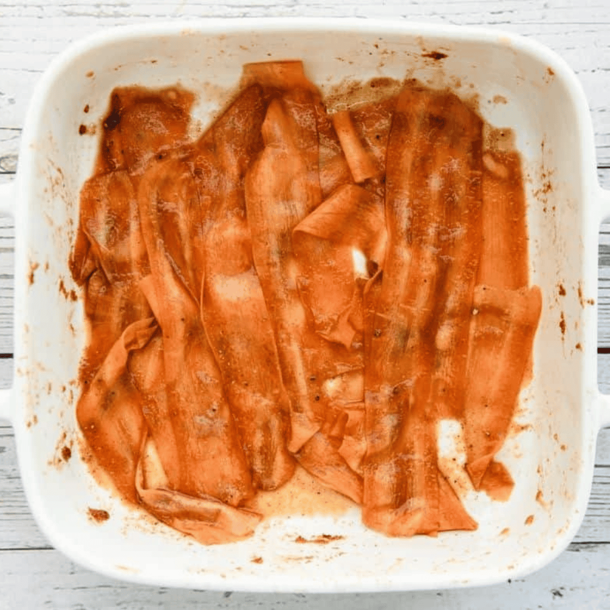 Thin carrot strips in a container being coated with a smoky maple marinade.