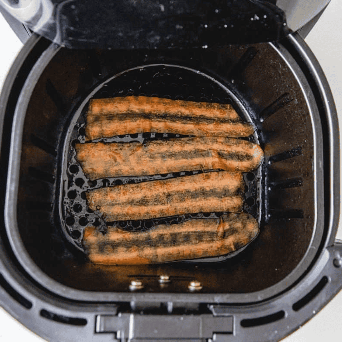 Carrot strips arranged in a sprayed air fryer basket, cooking to crispy golden perfection.