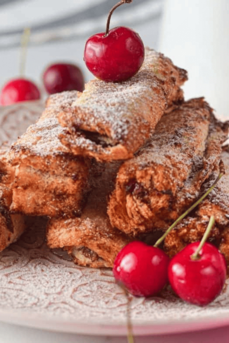 Golden-brown air fryer French toast stuffed with melted Nutella and warm cherries, served on a plate and dusted with powdered sugar.