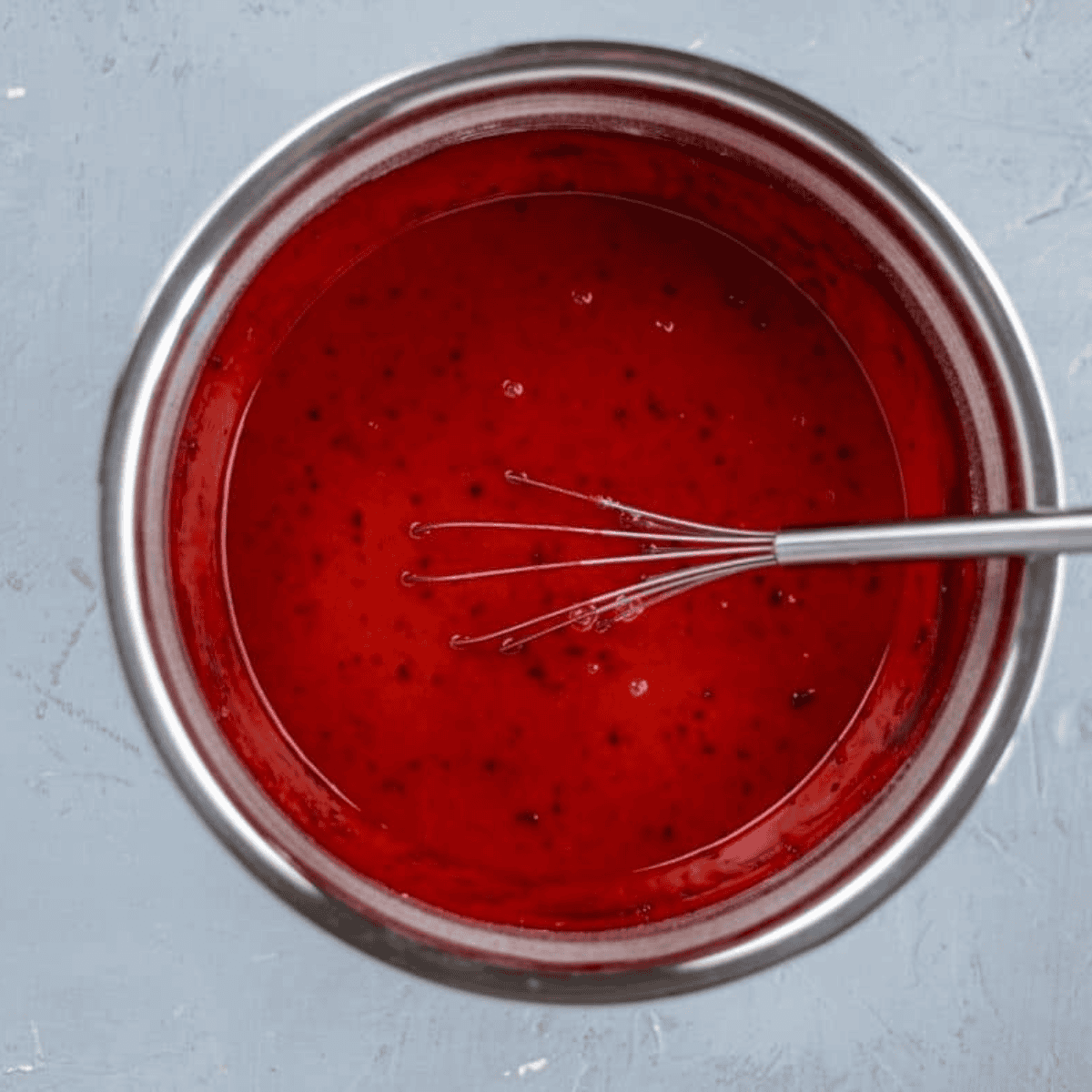 Mixing dry ingredients with flour, sugar, cocoa, salt, and baking soda, then combining wet ingredients including eggs, oil, buttermilk, vinegar, and vanilla, finally adding red food coloring to achieve vibrant red velvet cupcake batter.