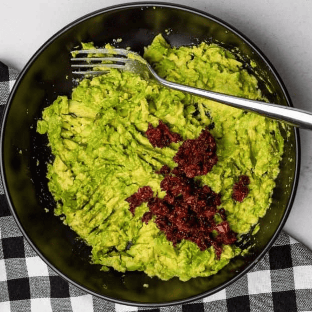Bowl of diced avocado, sun-dried tomatoes, red onion, and cheese being mixed gently