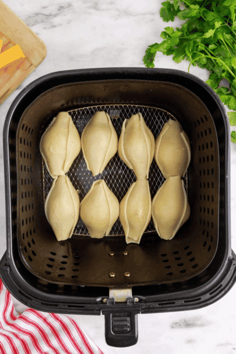 Stuffed taco pasta shells arranged in a single layer in an air fryer basket with space between each shell before cooking.