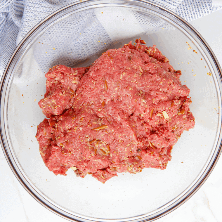Shaping seasoned ground beef into uniform patties on a cutting board.