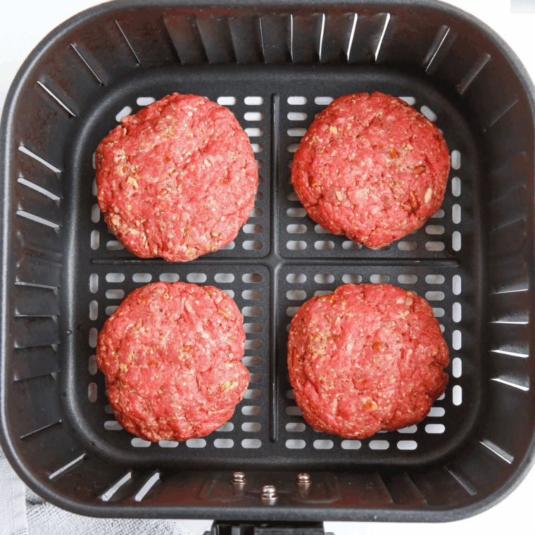 Beef patties arranged in a single layer inside an air fryer basket, cooking to a golden-brown finish.
