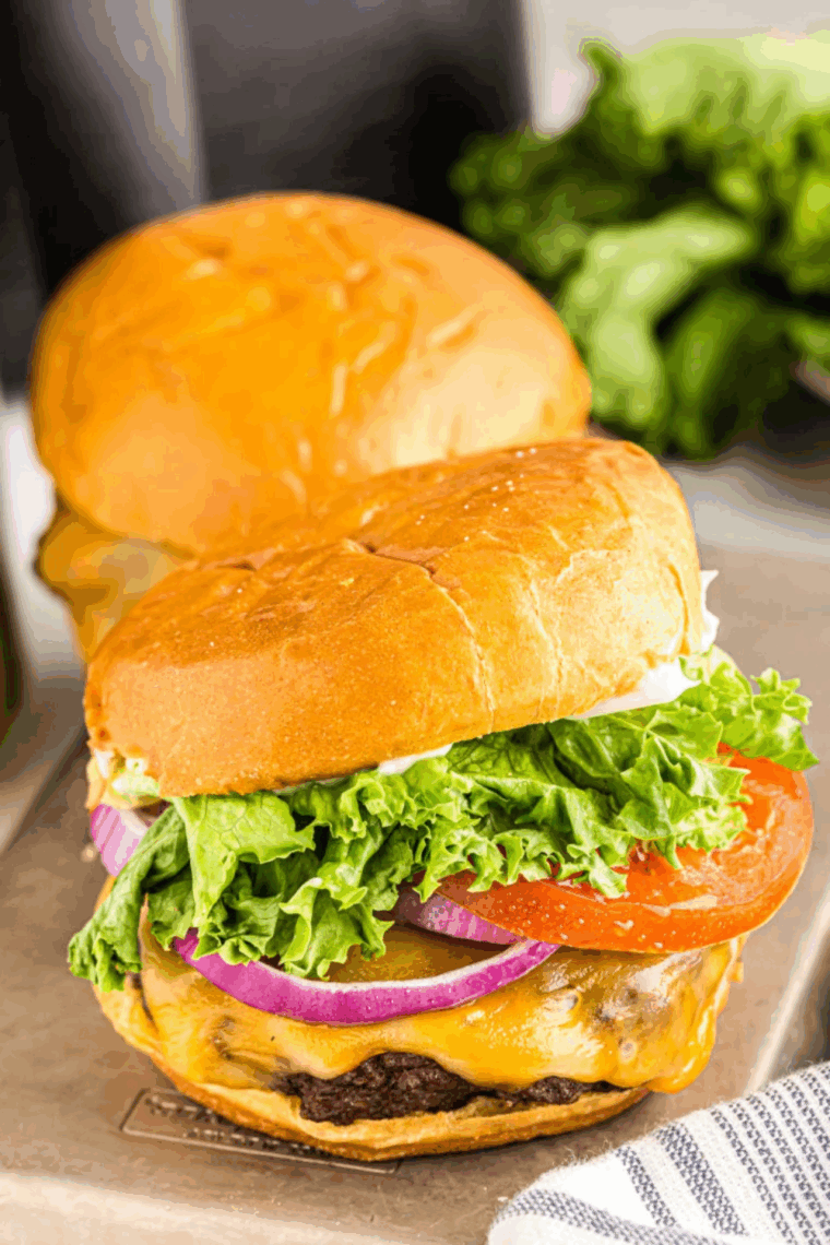 Close-up of a homemade Dairy Queen Flamethrower Burger with cheddar cheese, jalapeño sauce, lettuce, tomato, and pickles on a toasted bun.