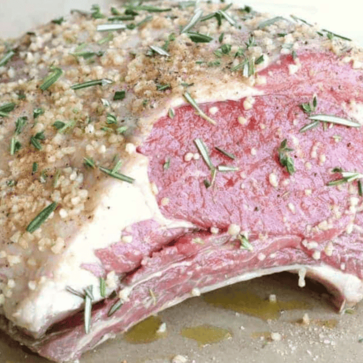 Preparing a prime rib roast by rubbing it with a savory mixture of olive oil, crushed garlic, rosemary, and seasoning.