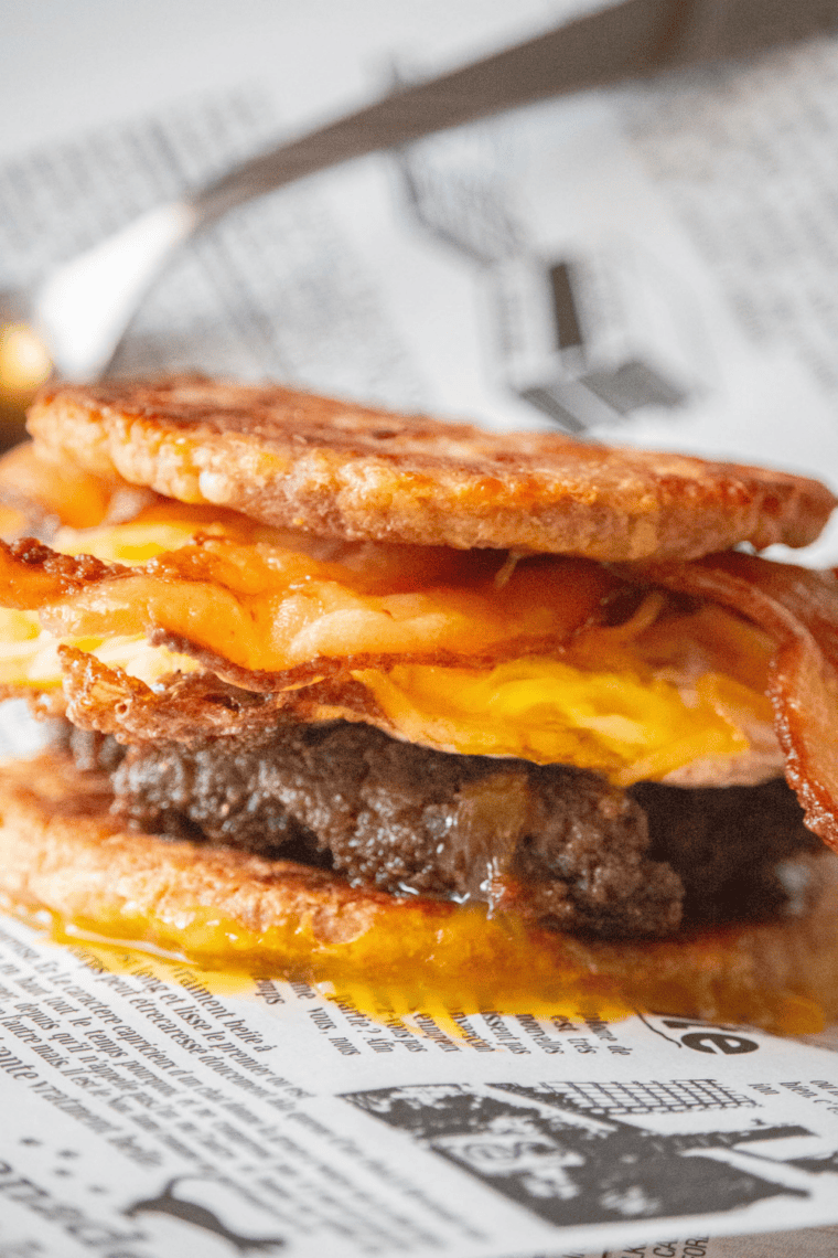Keto copycat sausage McGriddle assembled with a sausage patty, fried egg, melted cheese and bacon between two fathead dough buns
