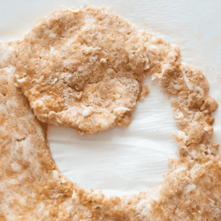 Fathead dough pressed flat between parchment paper with round McGriddle buns cut out using a biscuit cutter