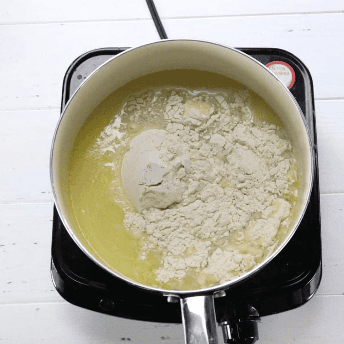 Stirring flour into hot butter mixture to form a smooth churros dough ball in a saucepan