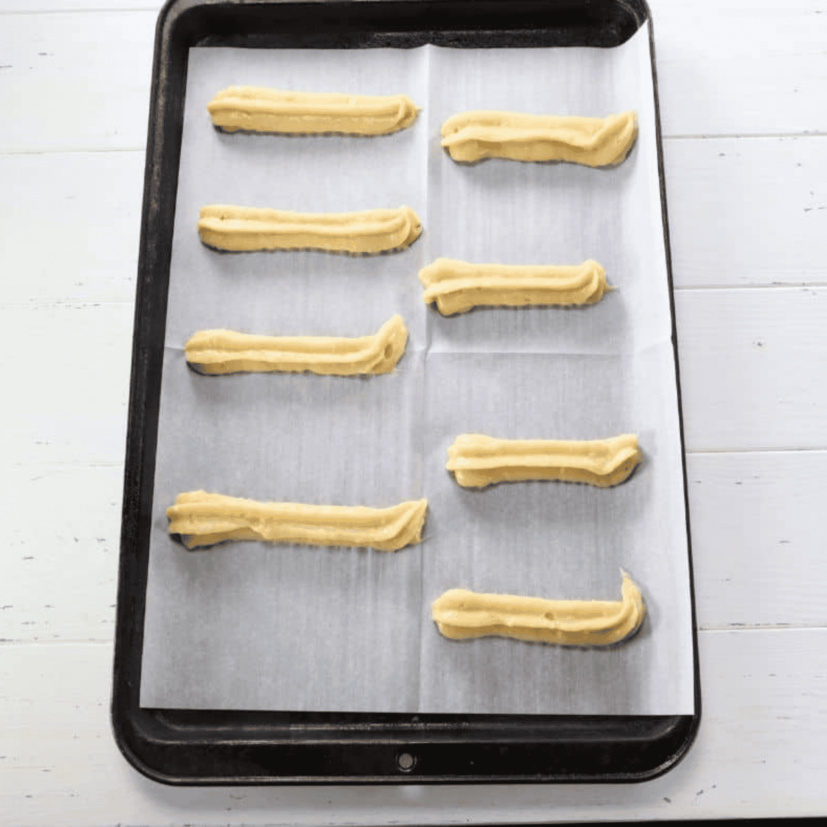Piped raw churros lined up on a baking sheet chilling in the refrigerator