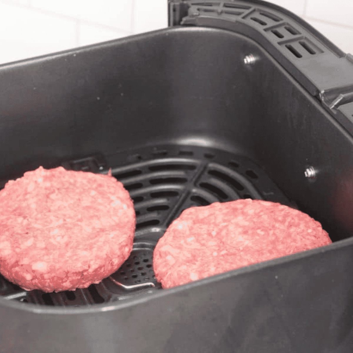 Hamburger patties cooking in an air fryer, flipped halfway through at 400°F