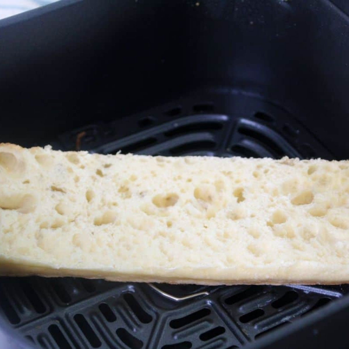 Halved baguette in air fryer basket toasting until golden brown.