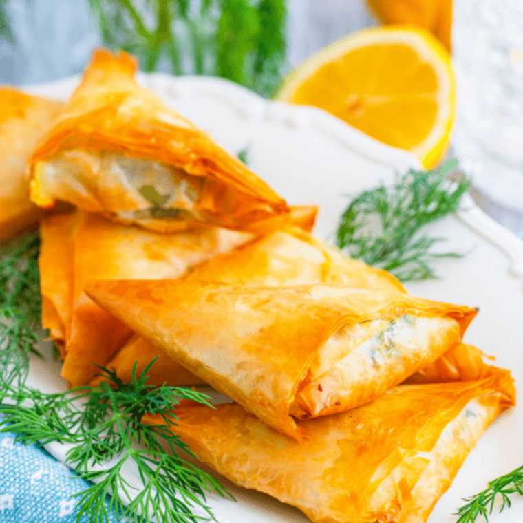 Golden air fryer spanakopita triangles filled with spinach, feta, and ricotta on a serving plate.
