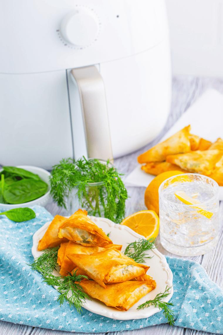 Crispy golden air fryer spanakopita triangles filled with spinach, feta, and ricotta on a serving plate.