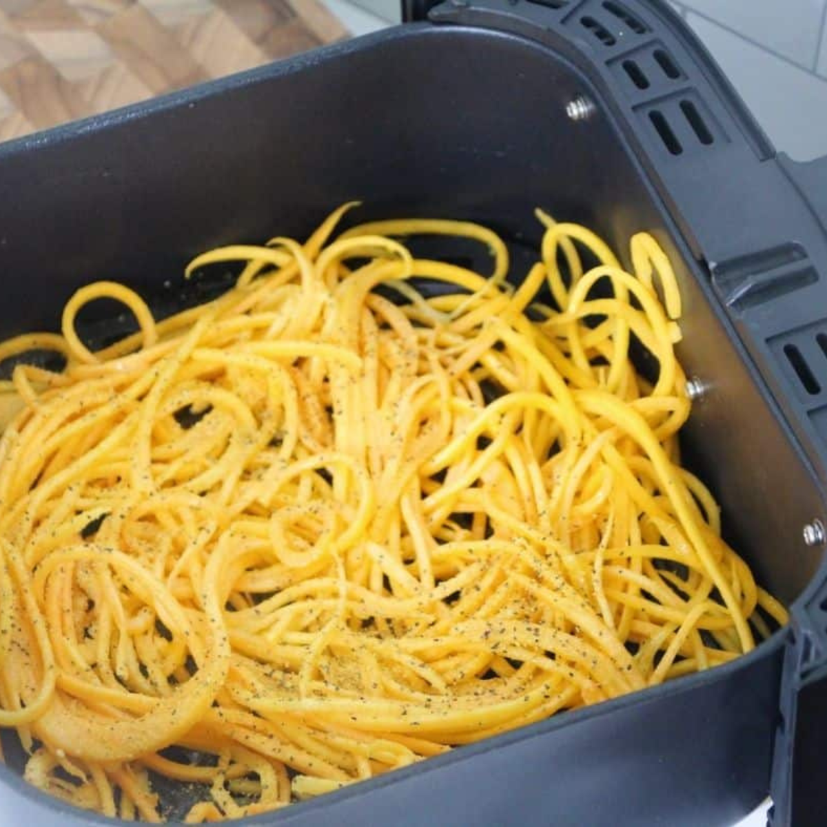 Butternut squash noodles tossed with olive oil and seasonings in a glass bowl