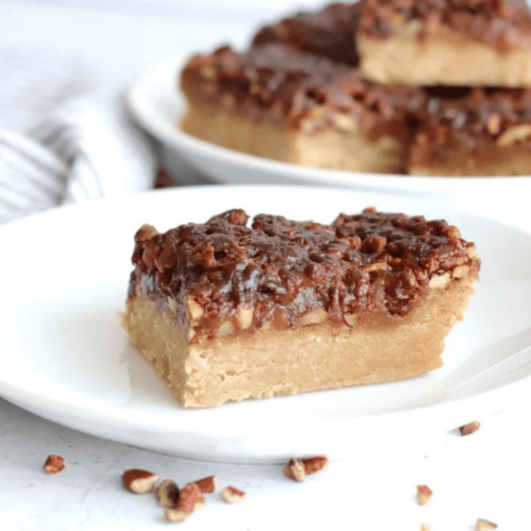 A white ceramic plate stacked with thick-cut Air Fryer Maple Pecan Bars, showing the golden-brown shortbread crust and a glistening, gooey maple topping loaded with toasted pecan halves.