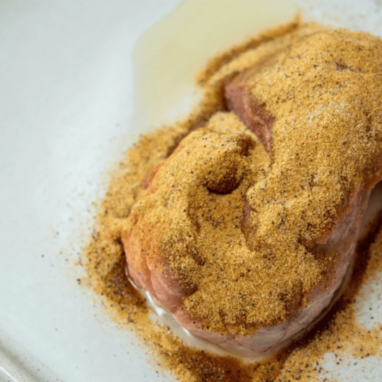 Cubed pork shoulder tossed in orange juice marinade with garlic and bay leaves in a glass bowl