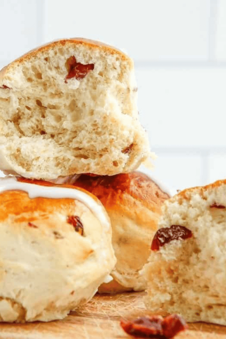 A close-up shot of golden brown air fryer hot cross buns with white flour crosses and a shiny apricot glaze, arranged in a black air fryer basket on a marble countertop.