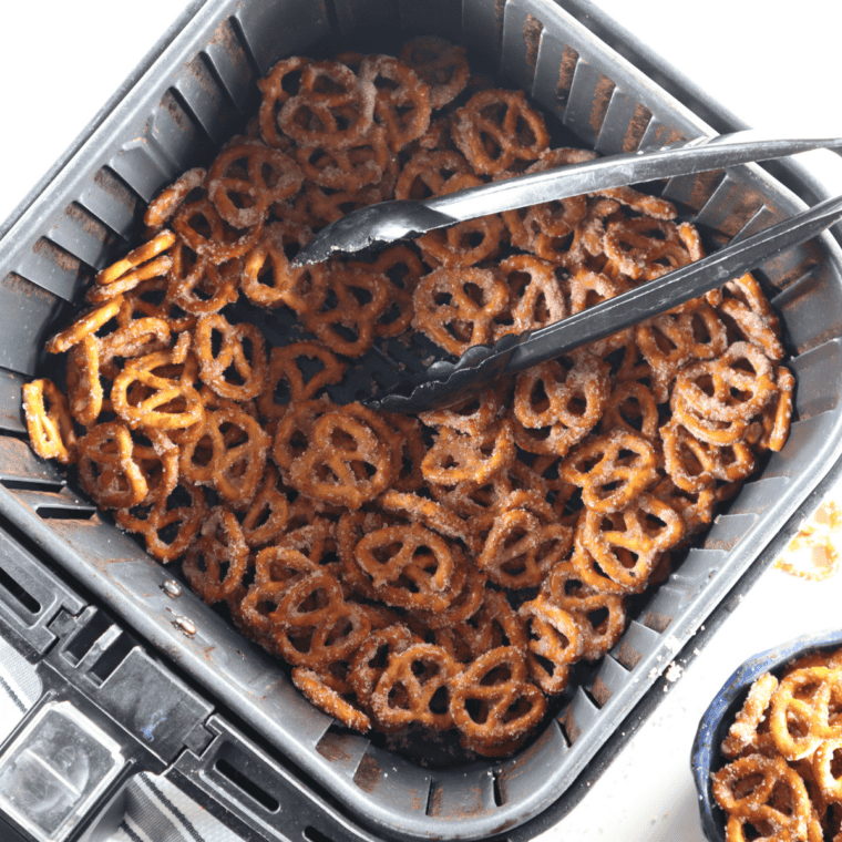 Cinnamon sugar pretzels in the air fryer basket with tongs resting on top.