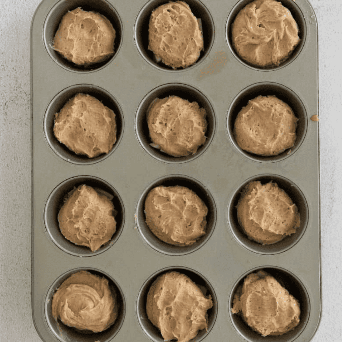 Spoon cake batter gently over apple slices in muffin tins, filling each cup three-quarters full while keeping apples in place for Easy Amish Apple Cake.