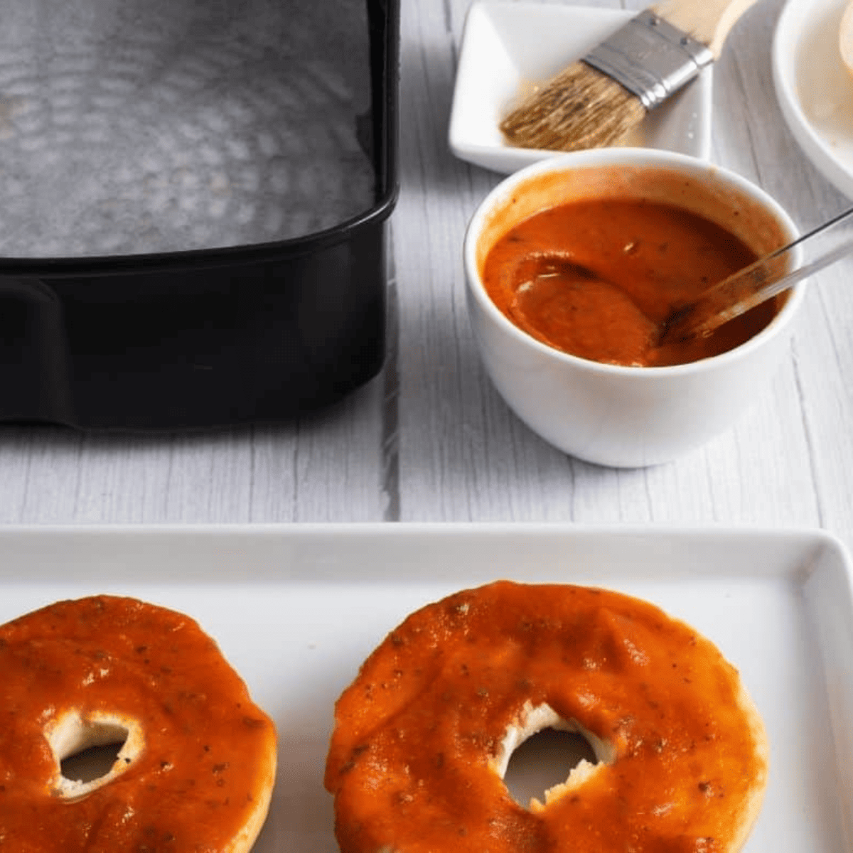 Bagel halves topped with an even layer of marinara sauce.