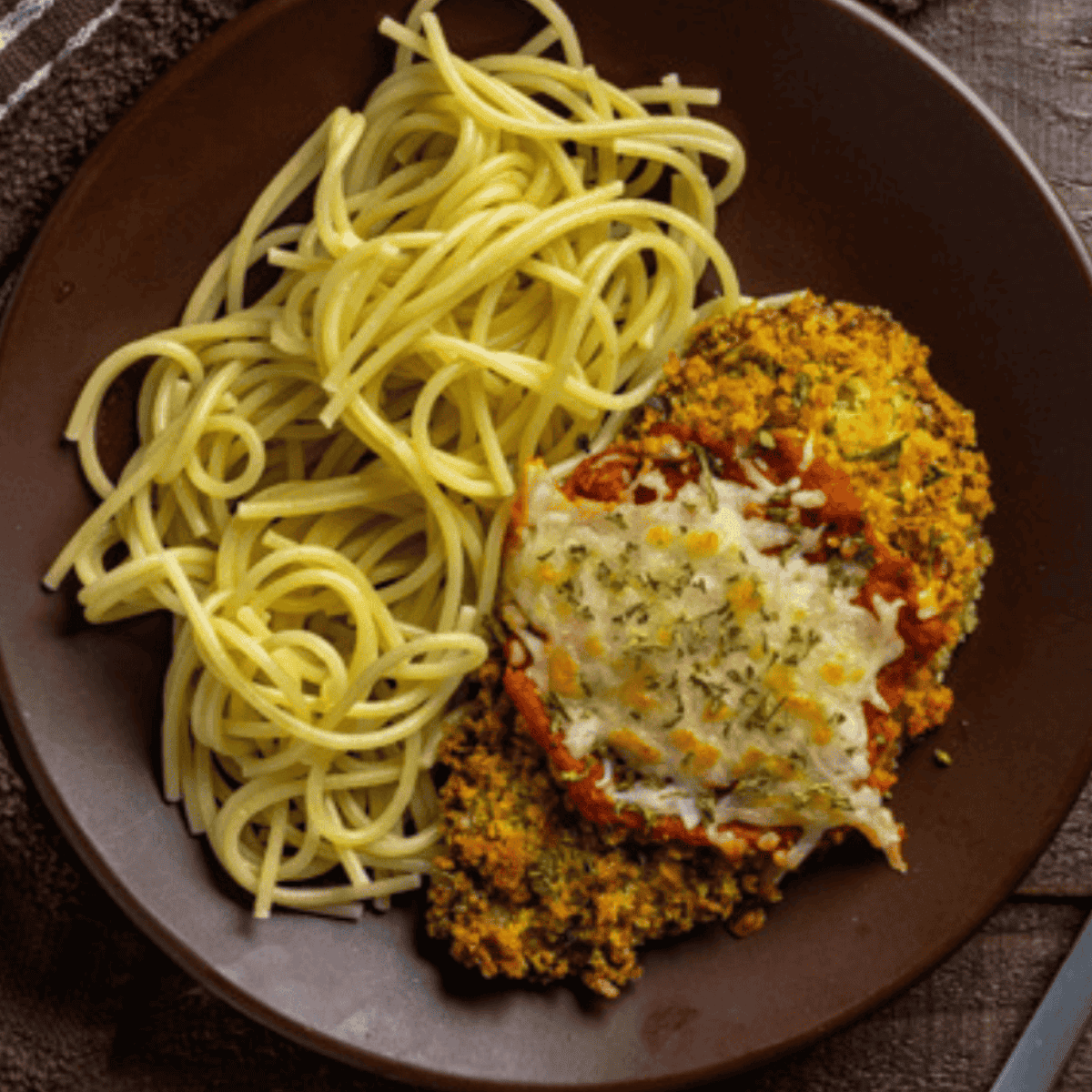 Crispy Easy Air Fryer Veal Parmesan cutlet topped with melted mozzarella cheese and marinara sauce on a plate.