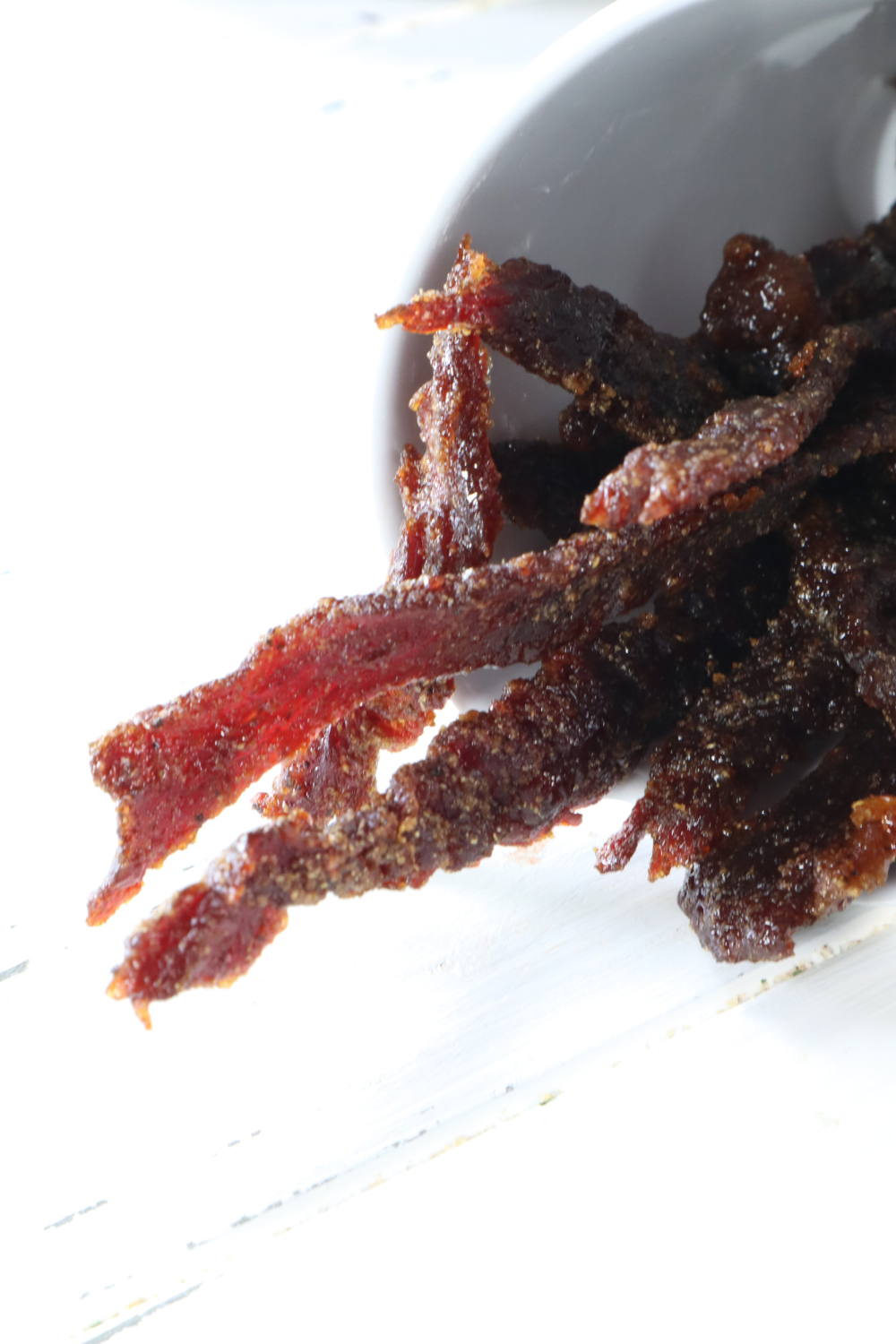 Overhead flat lay of finished air fryer beef jerky next to soy sauce, garlic, and brown sugar ingredients on a slate background